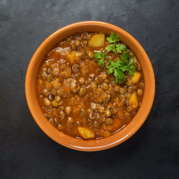 Hearty lentil stew with potatoes and fresh parsley in an orange bowl on a dark background.
